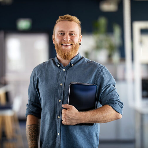 Ein junger Mann mit Bart und Tablet unter dem Arm in einem Büro