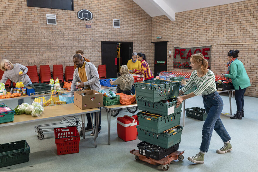 Acht Menschen in einer Turnhalle sortieren Lebensmittel, verteilen diese auf die bereitgestellten Tischen und treffen die letzten Vorbereitungen für die ersten Kunden.