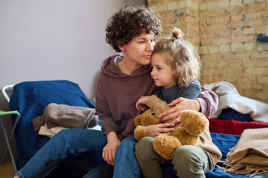 Eine junge Frau umarmt ihren kleinen Sohn, der einen braunen Teddybär in der Hand hat.