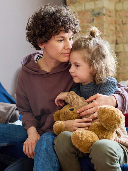 Eine junge Frau umarmt ihren kleinen Sohn, der einen braunen Teddybär in der Hand hat.